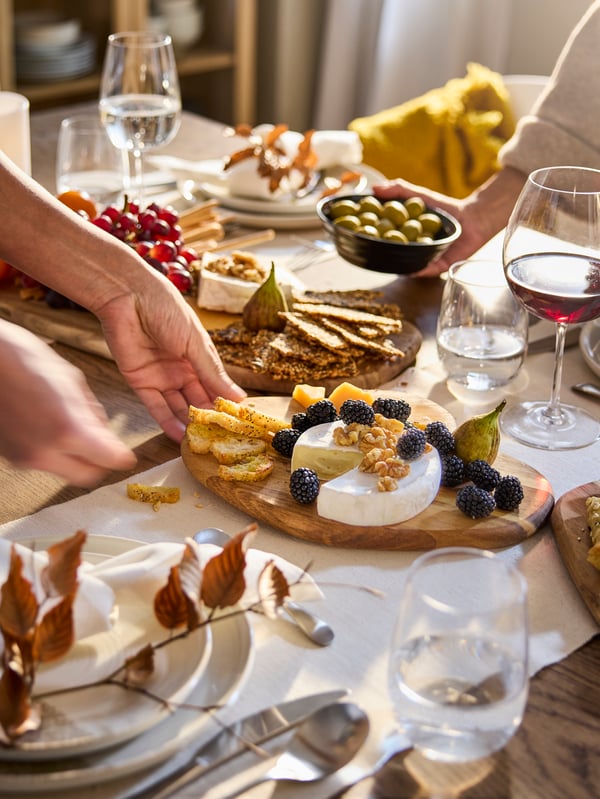 Hand placing a wooden cutting board filled with appetizer on a dining table with other food and dishware.