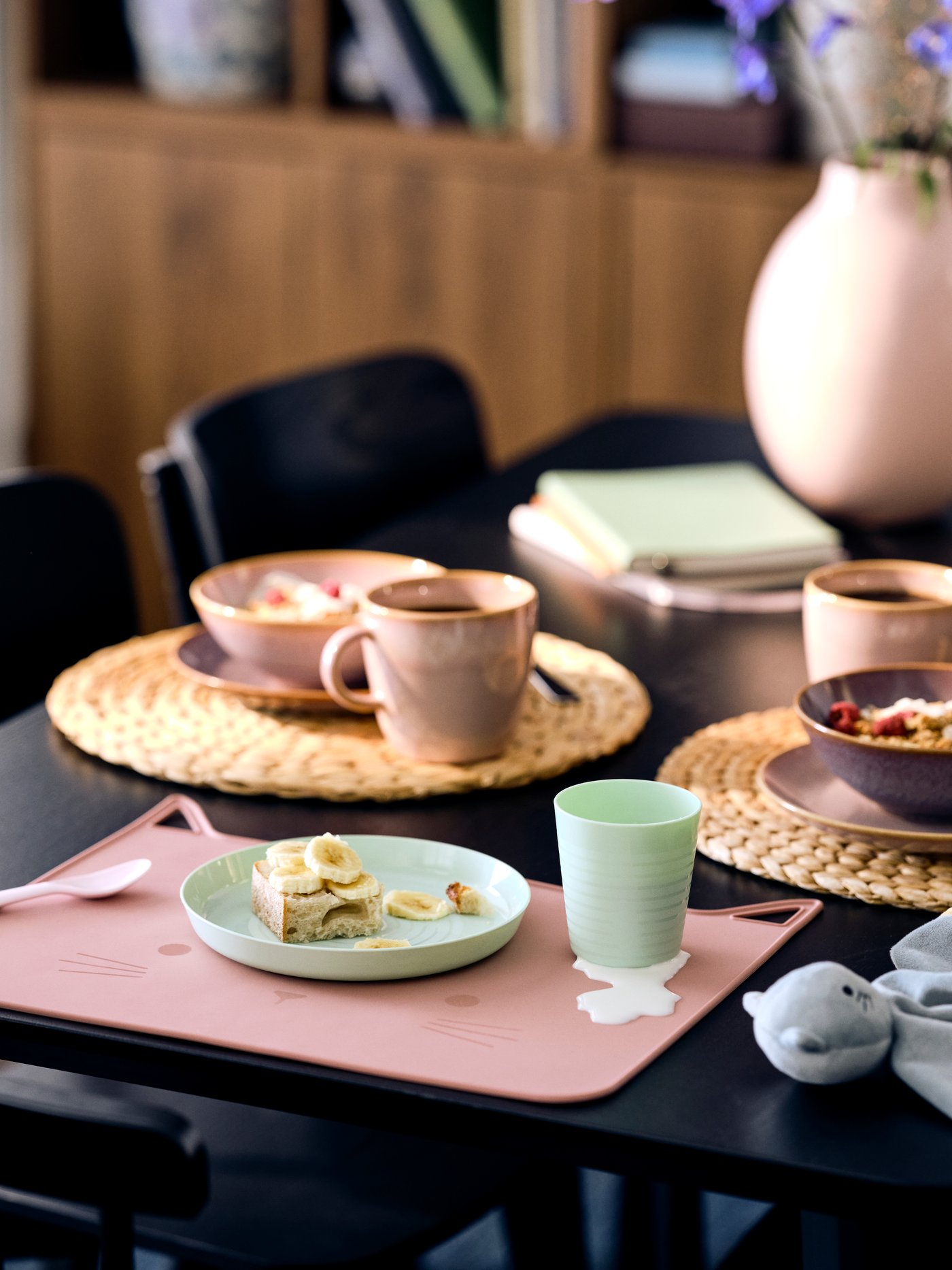 A black LISABO table set for a meal with FÄRGKLAR plates, mugs, pale pink GULDVÄVARE placemats and table runners. A look that’s both bold and soft — perfect for serving up style with every bite.