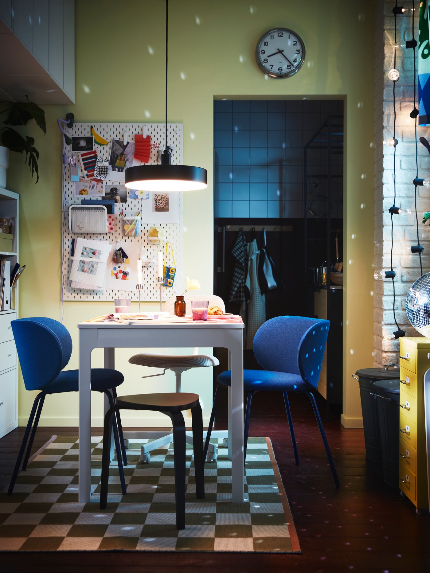 Tlumeně osvětlený jídelní kout vybavený rozkládacím stolem EKEDALEN a modrými židlemi KRYLBO. Na stěnách tančí světlo, které se odráží od disko koule.