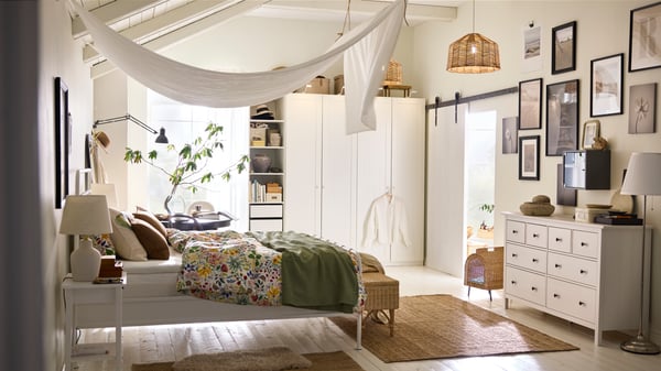 A white STJÄRNÖ bed covered in a floral pattern STRANDLUMMER bed linen with a DYTÅG curtain draped from the ceiling above it.