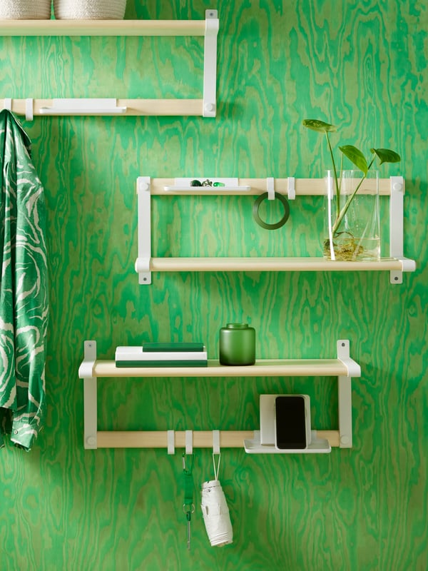 Three SKOMAKARE wall shelves in white and aspen mounted on a green-colored wall, holding keys and a mobile phone.