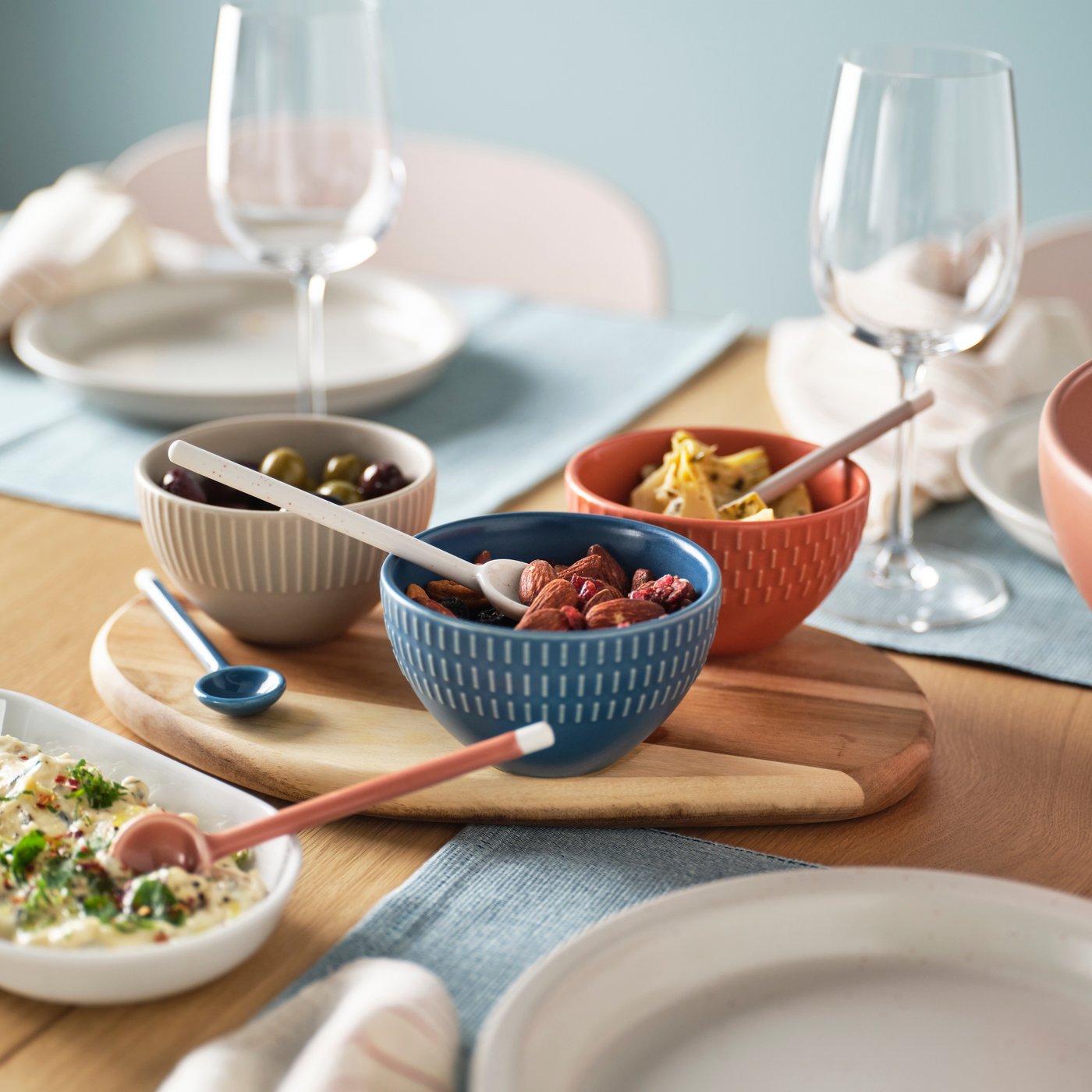 Trois petits bols colorés sur une FASCINERA planche à découper au milieu d’une table dressée pour le souper.