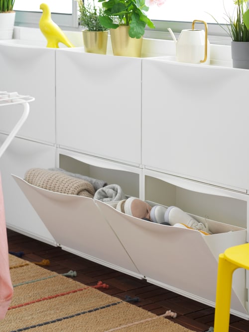 Wand eines geschlossenen Balkons/Wintergartens mit weißen TRONES Aufbewahrungen aus Kunststoff, in denen saisonale Kleidung aufbewahrt ist.