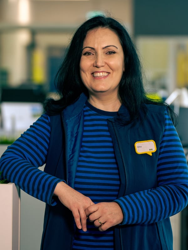 Silva in her blue work wear standing in the back-office smiling.