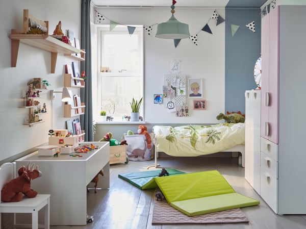Ett ljust barnrum med blåa, rosa och gröna inslag där sängen är bäddad med ett grönt dinosauriepåslakanset och en mjukdjurs-dinosaurie sitter på en stol i framkant av bilden.