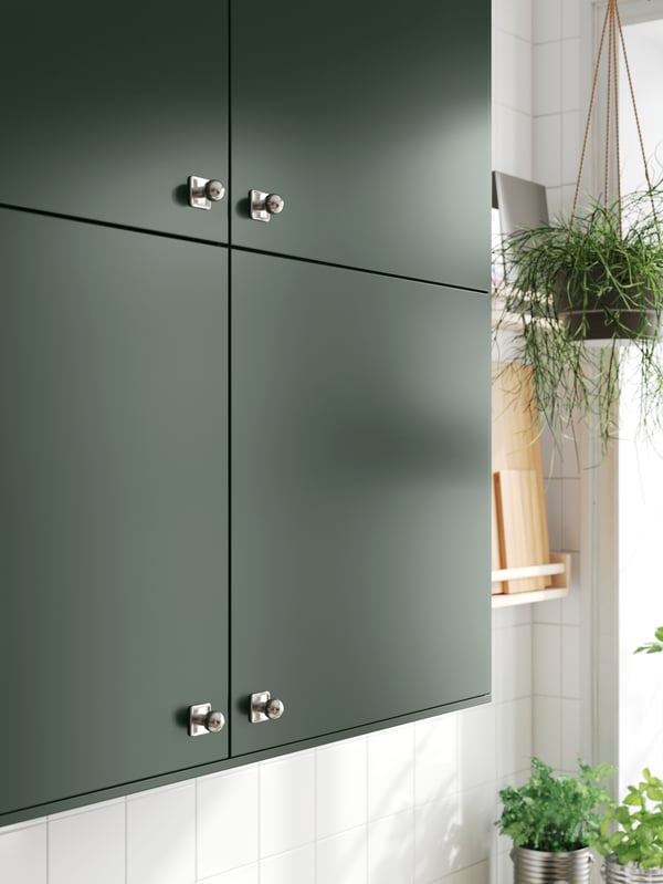 Wall cabinets with deep green HAVSTORP kitchen fronts and stainless steel SÖRBYN knobs, on a white-tiled wall.