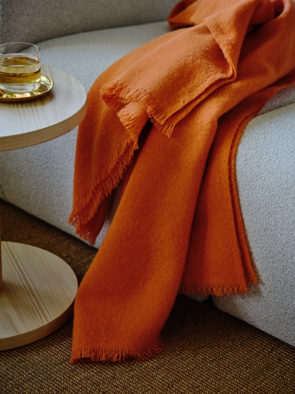 Eine orangefarbene Decke liegt über der Armlehne eines hellen Sofas.