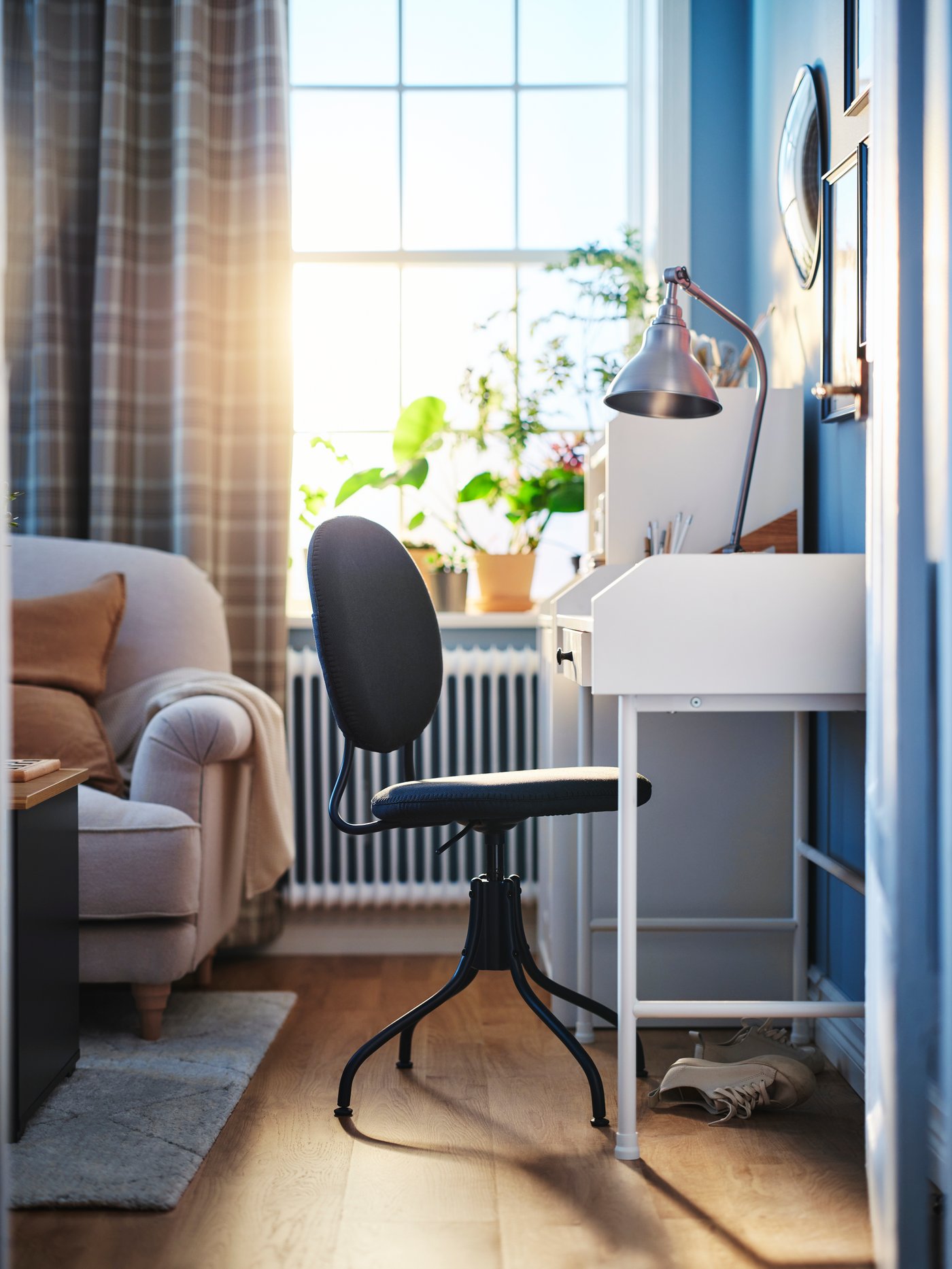 Ein blauer BJÖRKBERGET Drehstuhl steht an einem weissen HAUGA Schreibtisch mit einer ANKARSPEL Arbeitsleuchte in Zinneffekt.