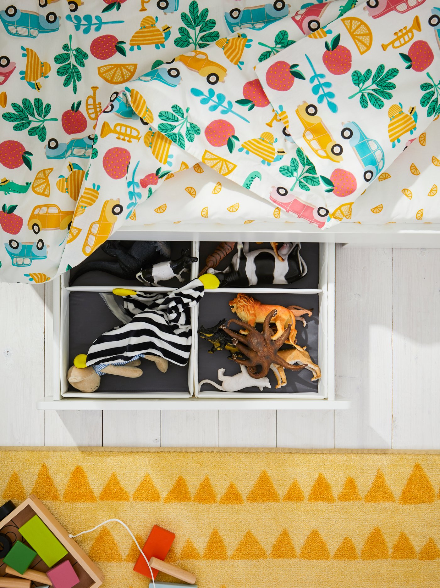 מגירה שלופה מתחת למיטת תינוק STUVA/FRITIDS. בתוכה מסודרים צעצועים בקופסאות RASSLA עם תאים.