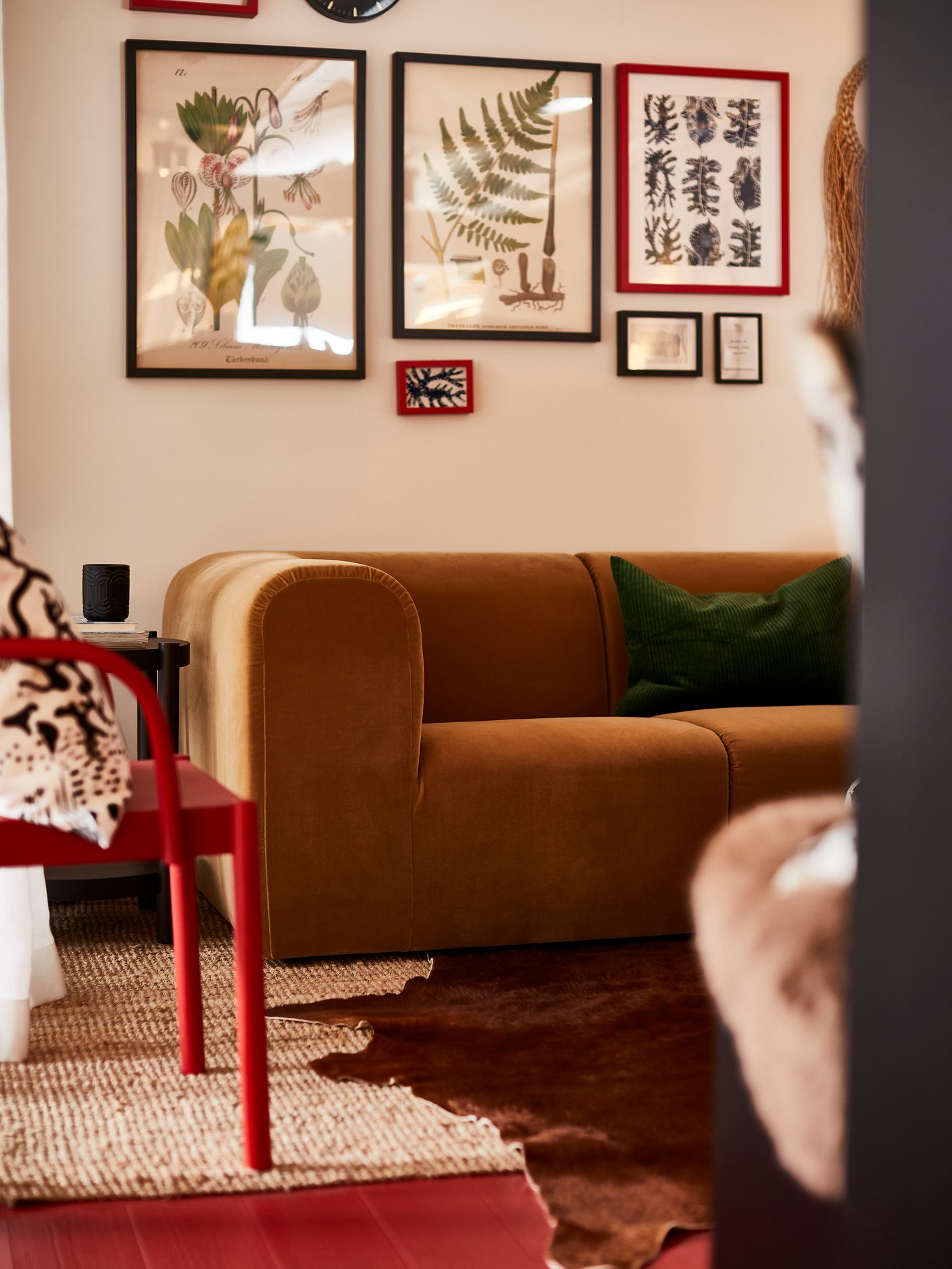 Ein braunes Sofa steht im Wohnzimmer vor einer Bilderwand und daneben steht ein roter Stuhl.