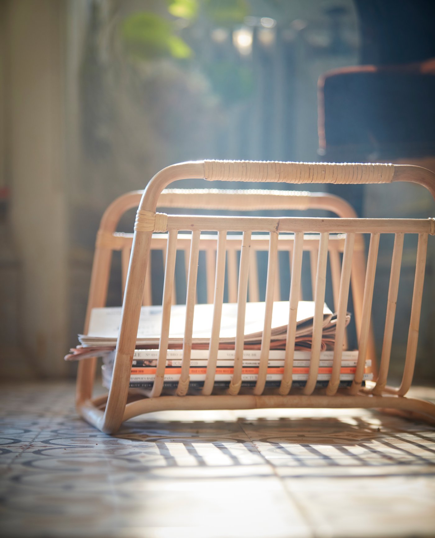 Un primer pla del porta-revistes BUSKBO fet a mà amb rotang, col·locat a terra i amb unes quantes revistes.