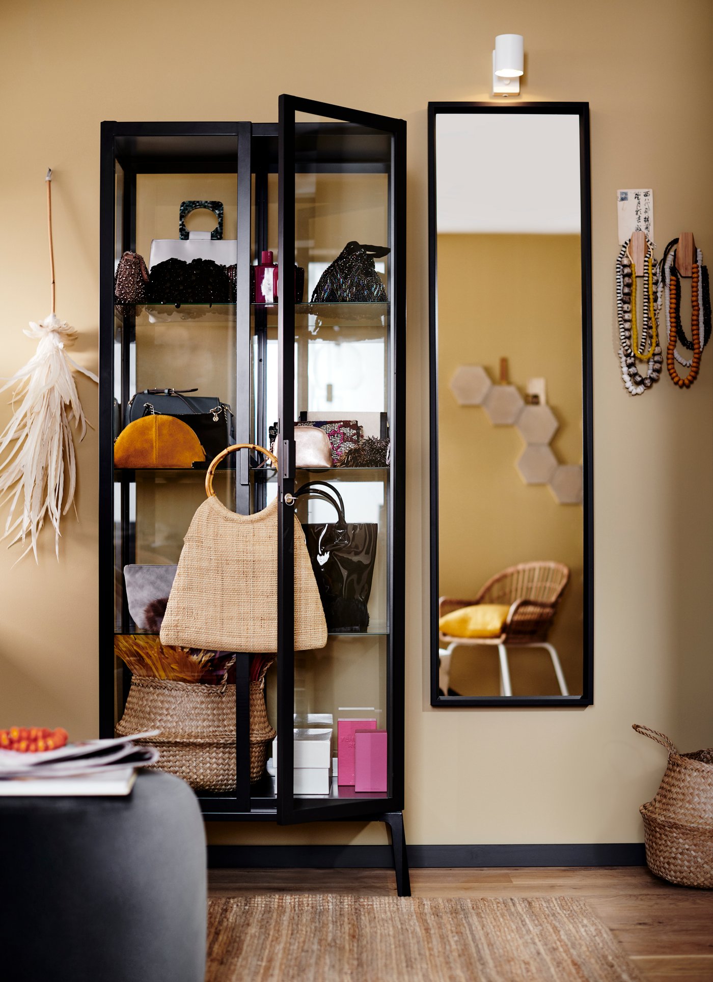 Eine Vitrine mit einer Vielzahl verschiedener Gegenstände, u. a. Handtaschen, steht neben einem Spiegel an einer Wand.