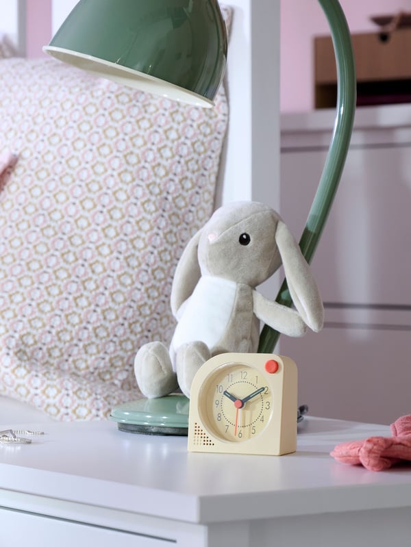 Close-up of bedside table with TJINGA alarm clock, DVÄRGHARE soft toy rabbit and RÖDFLIK desk lamp.