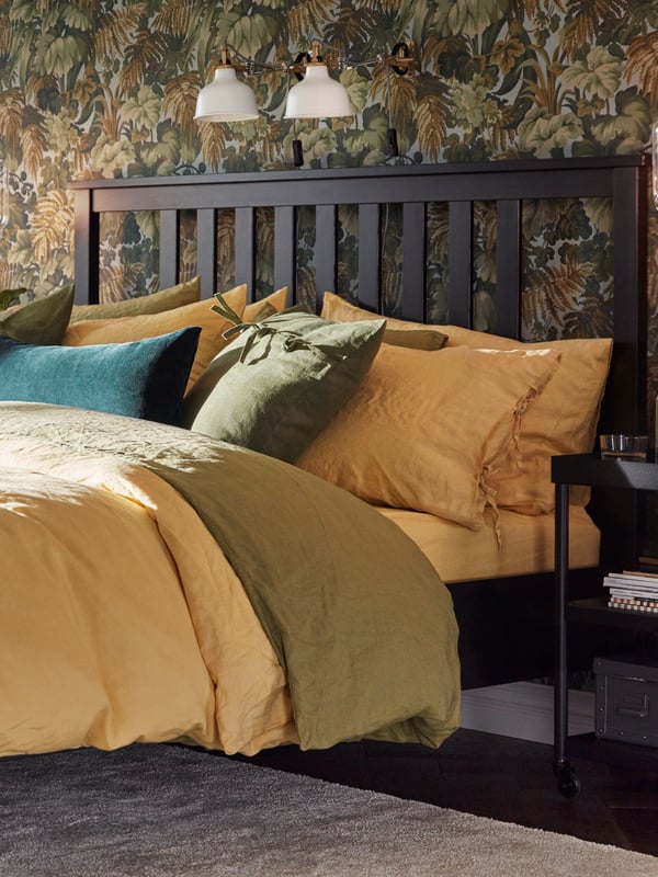 A HEMNES bed with yellow and green PUDERVIVA quilt covers and pillowcases, a yellow sheet and a green velvet cushion.