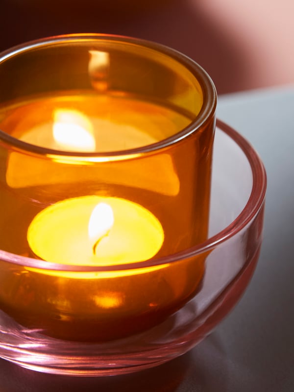 Närbild på TALLTITA ljushållare i rosa och orange glas. 