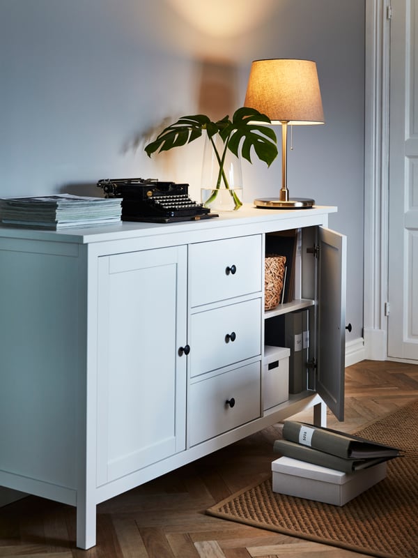 HEMNES sideboard with a lamp and various items on top. A door ajar with boxes and binders stored within.