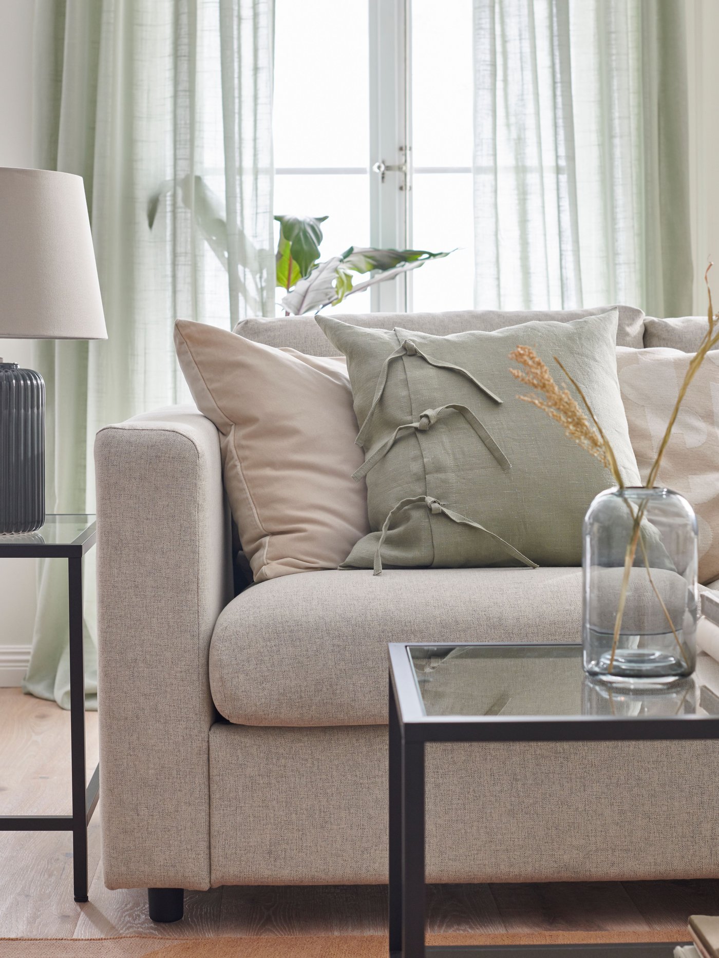 Cortinas translúcidas SILVERLÖNN de color verdehasta el suelo detrás de un sofá VIMLE