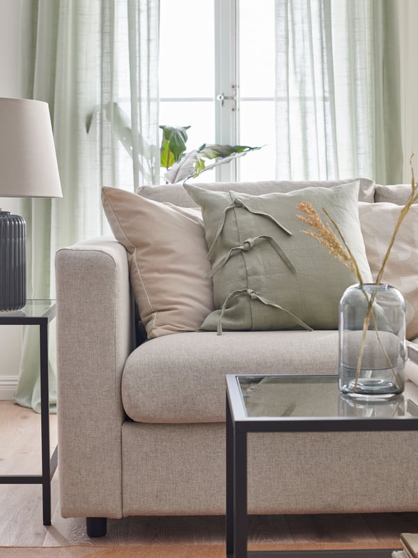 Cortinas translúcidas SILVERLÖNN de color verdehasta el suelo detrás de un sofá VIMLE