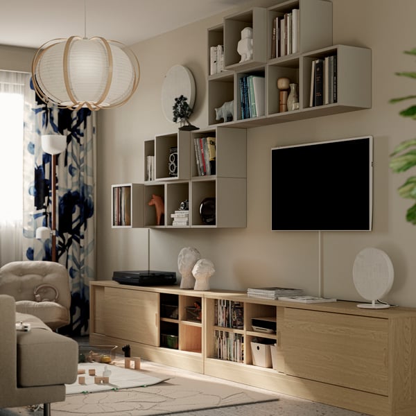 A lot of different EKET cabinets and a TV are attached to a wall above two oak veneer TONSTAD TV benches in a living room.