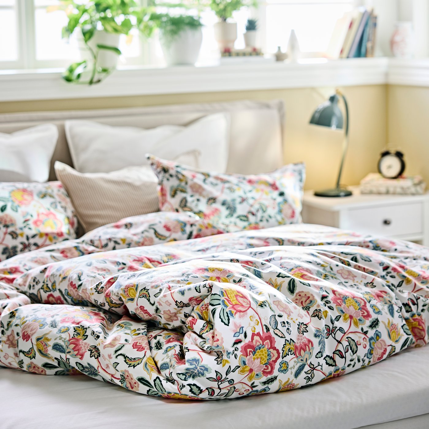 DAGSSALVIA duvet cover with a floral pattern spread across a bed in a bedroom with cushions and decor on a window sill.