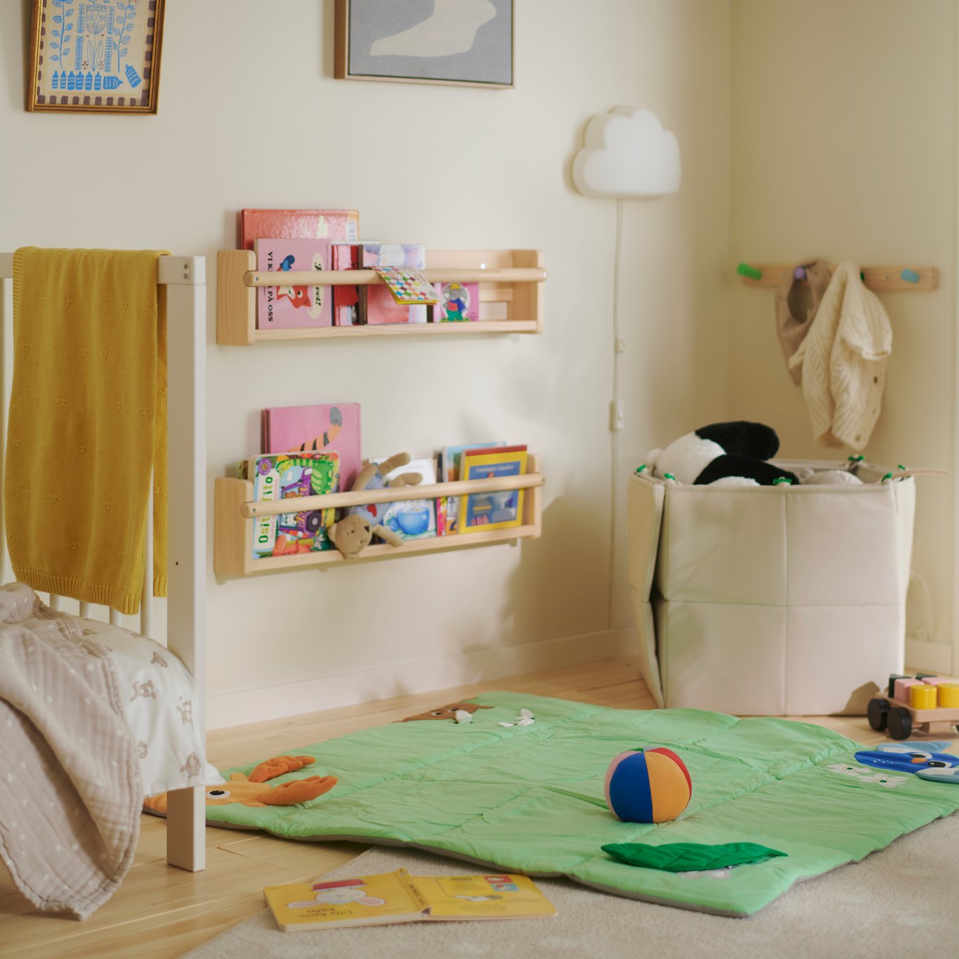 A neutral children’s room with a green SANDI play mat, toys and books on the floor, and bookshelves mounted on the wall.