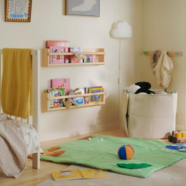 A neutral children’s room with a green SANDI play mat, toys and books on the floor, and bookshelves mounted on the wall.