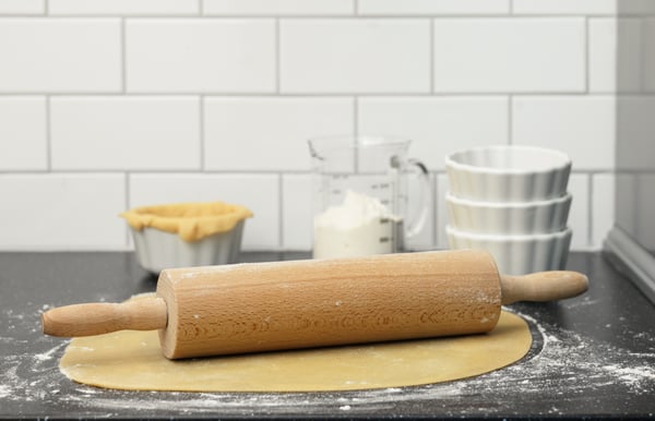 Detalle de un rodillo de amasar colocado sobre una base de pizza en una encimera de cocina.