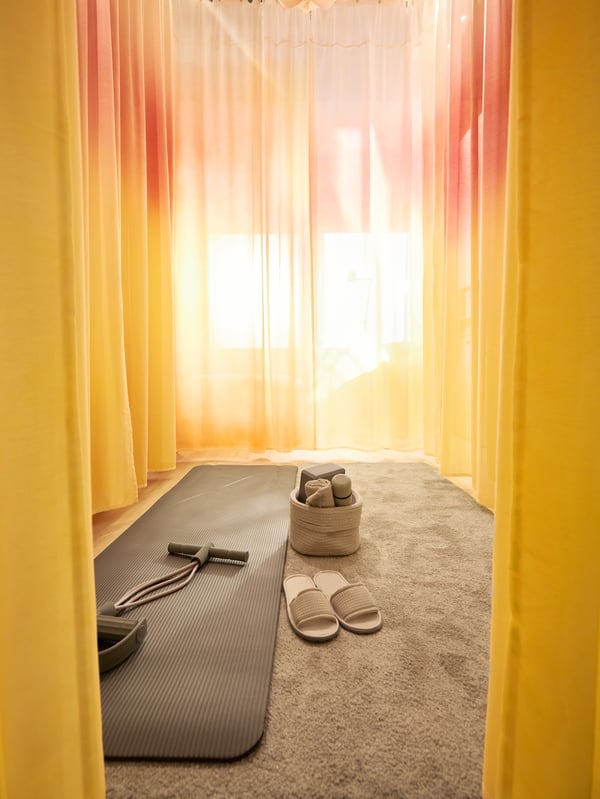 Gelbe und rosafarbene Gardinen sind so aufgehängt, dass ein ruhiger Bereich mit einer Yoga-Ausrüstung entsteht.