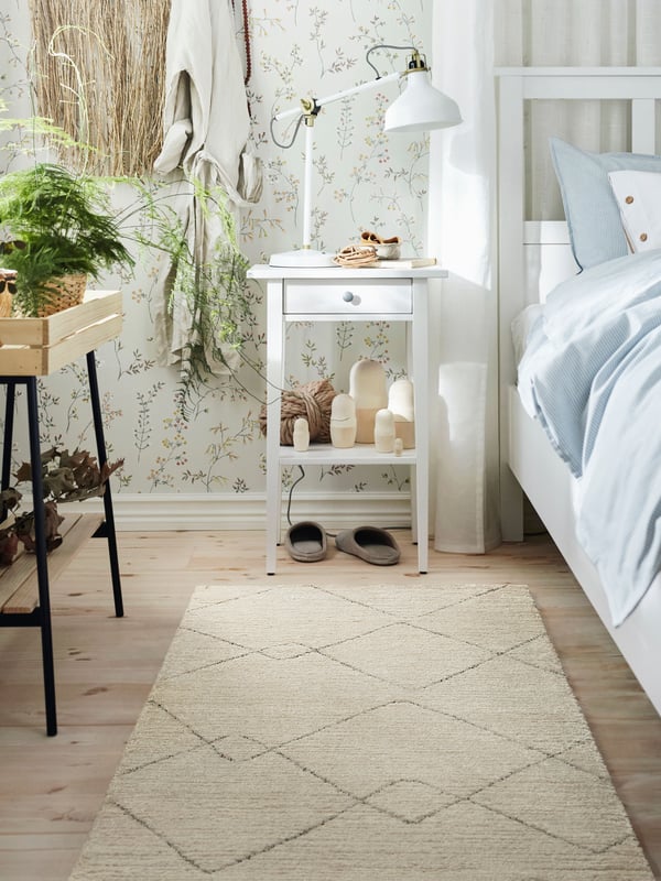 Valkoinen TVERSTEDT-matto makuuhuoneen lattialla. Takana HEMNES valkoinen yöpöytä.