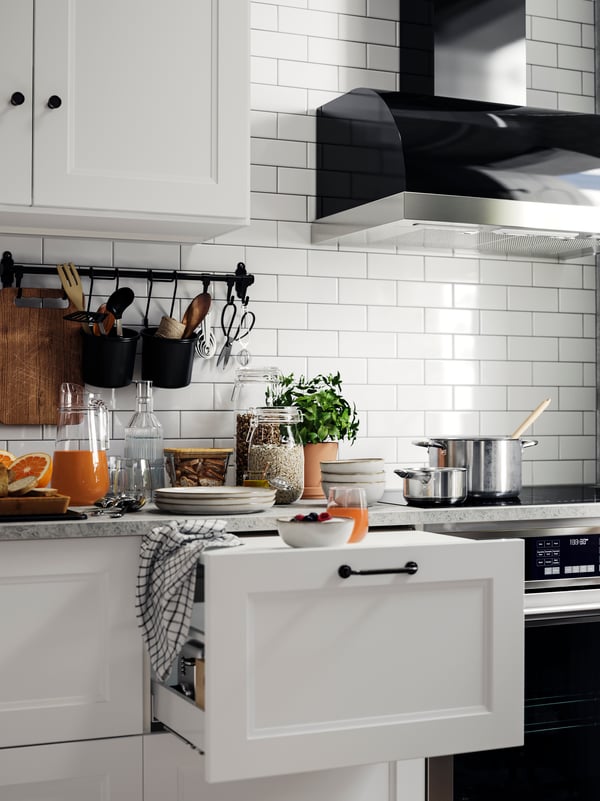 AXSTAD matte white kitchen fronts with a drawer partially open, and a countertop set with juice, a bowl of fruit.