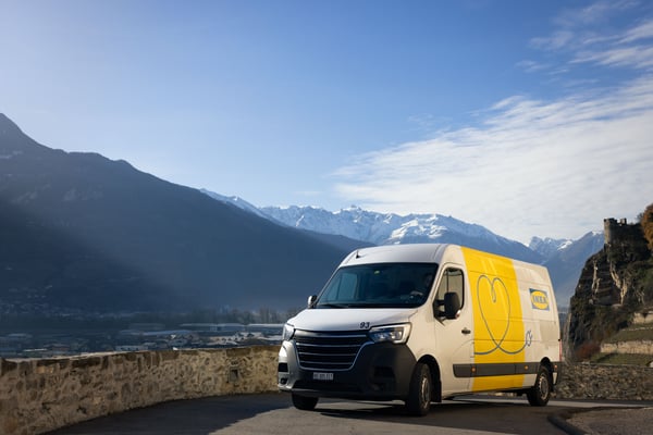 Un veicolo elettrico per le consegne IKEA su una strada in Svizzera, con il cielo azzurro e una catena montuosa parzialmente innevata sullo sfondo.