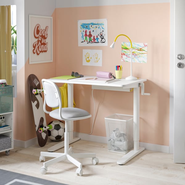 A white RELATERA sit/stand desk, a desk chair in white and grey in a room with light orange walls and posters on the wall.