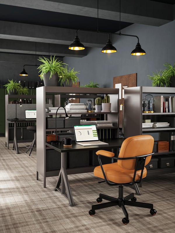 A black/dark grey IDÅSEN desk and light brown leather chair with a built-in shelf and room divider shown next to several desks.
