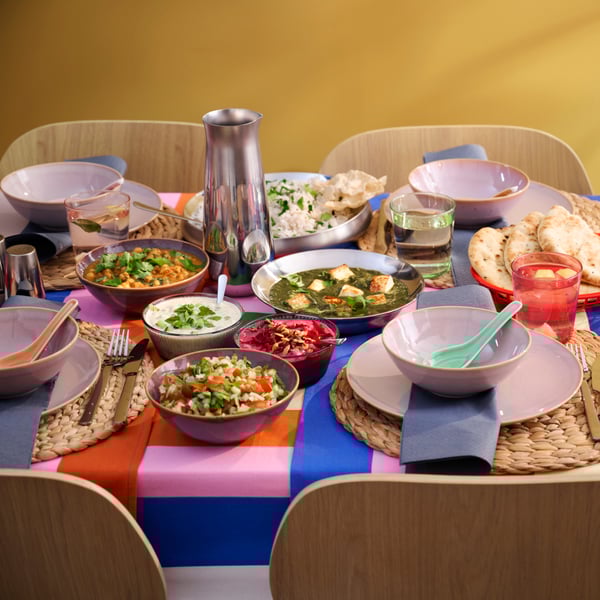 Une table est recouverte d'une nappe aux motifs colorés, sur laquelle sont posés des bols et des assiettes colorés remplis de nourriture.