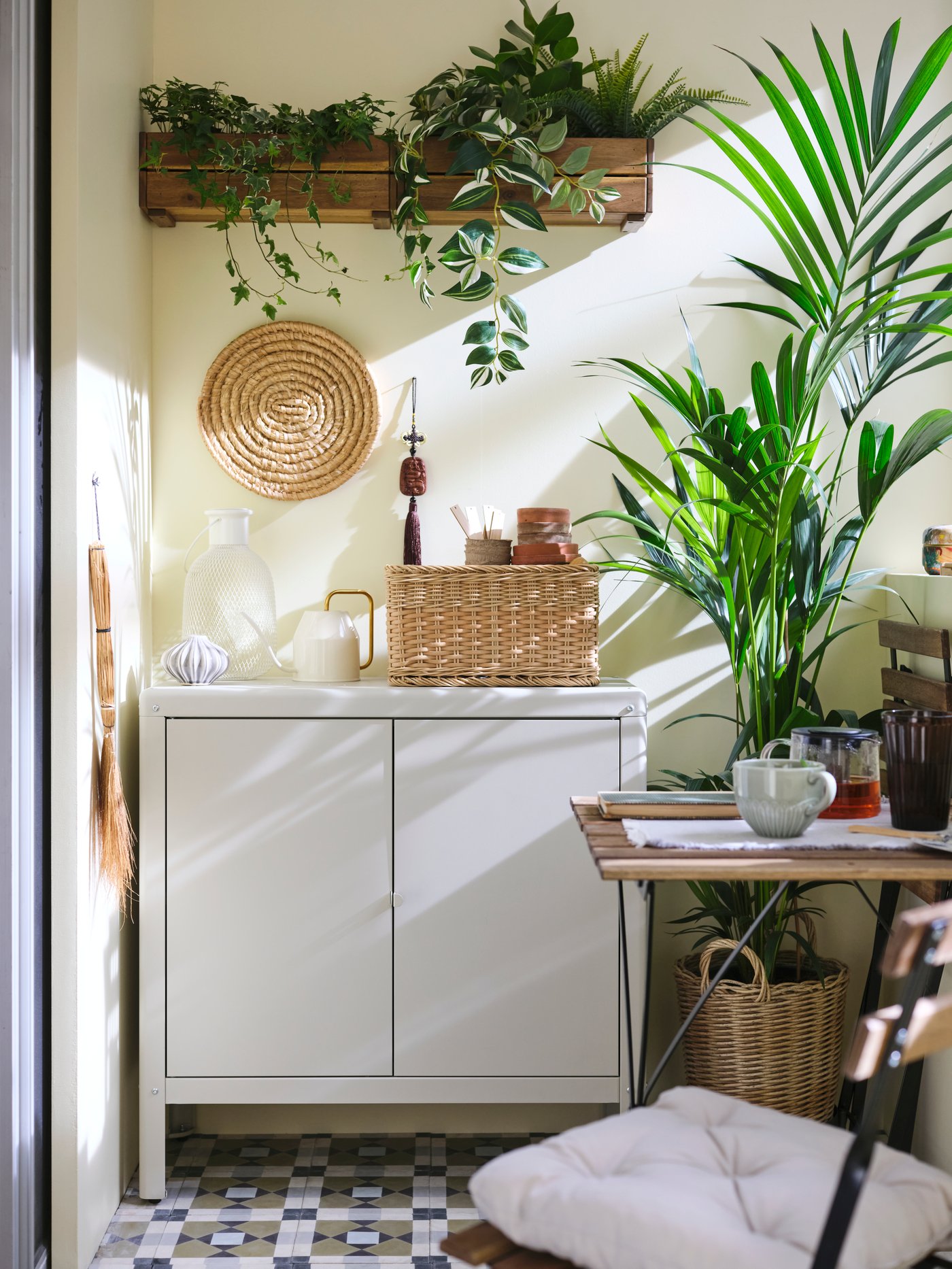 Sur un balcon fermé, un rangement d’intérieur/extérieur KOLBJÖRN beige en acier galvanisé où sont posées une lampe portative et une boîte d’outils de jardinage.