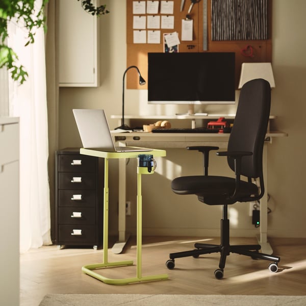 Laptopständer neben einem dunkelgrauen SMÖRKULL Bürostuhl mit Armlehnen, neben einem Schreibtisch und Pflanzen an der Wand.