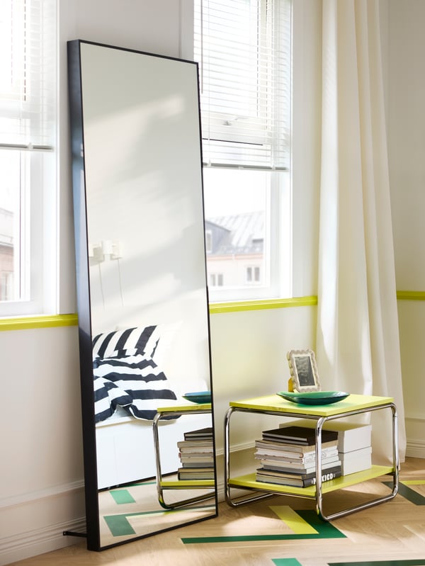 HOVET mirror between two windows, with BAGGBODA side table next to it and a reflection of a bed in the mirror.