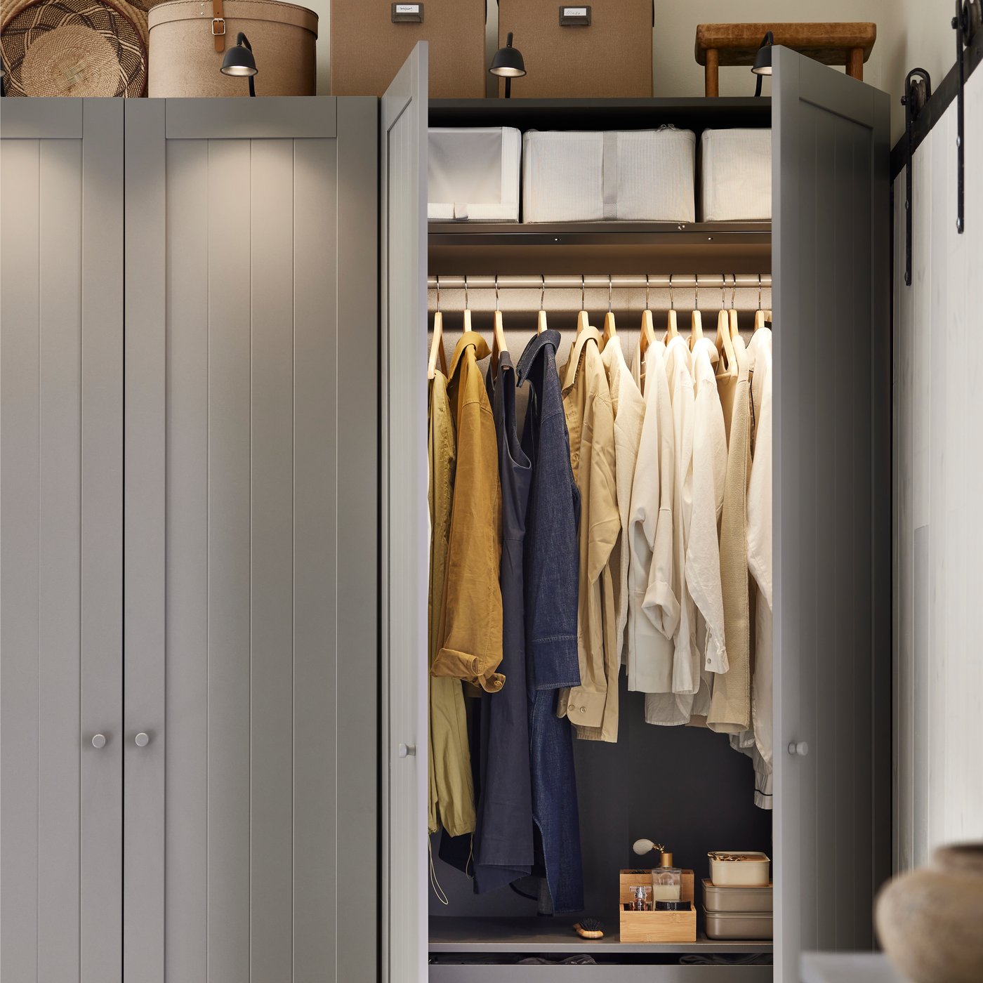 Ett sovrum med en PAX/GULLABERG garderobskombination med hängande kläder och förvaringskorgar ovanför.