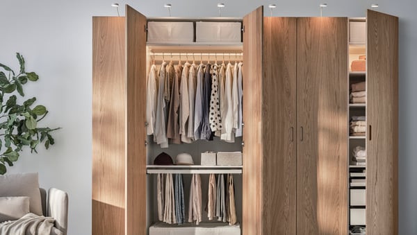 A PAX wardrobe with six oak veneer TONSTAD doors, three of which are open showing clothes on hanging rails and shelves.