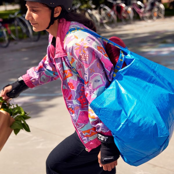 Person rollerskating wearing a helmet, an IKEA paperbag in one hand and a blue IKEA bag over the shoulder.