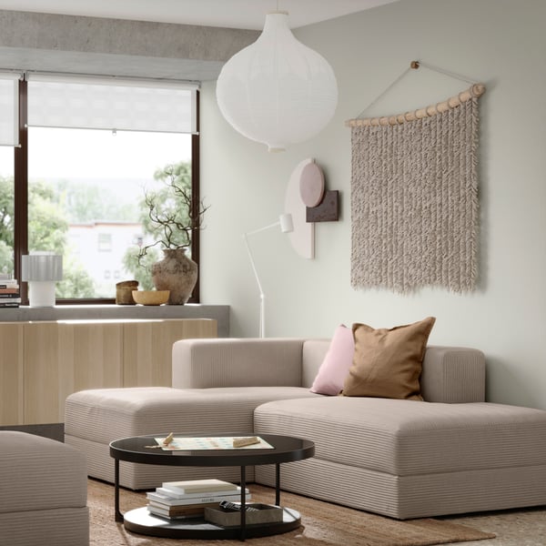 En Samsala grå-beige JÄTTEBO sjeselongmodul i en beige stue med et svart rundt FRÖTORP sofabord. 