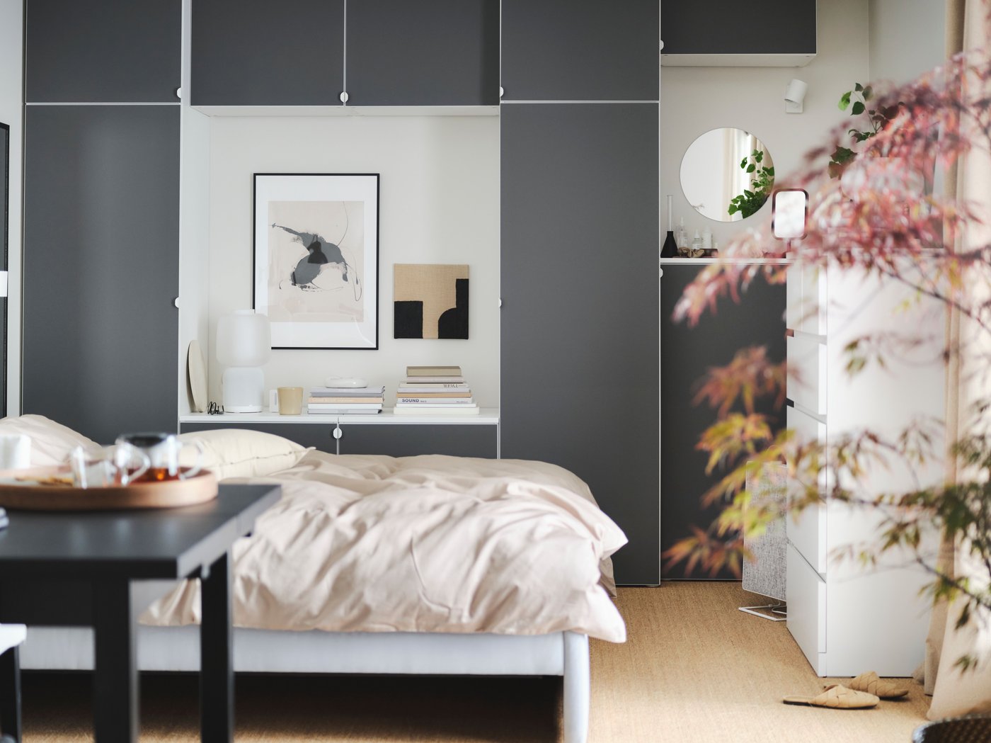 Una camera da letto tranquilla con un letto grande, una scrivania in legno, un guardaroba grigio dalla forma dinamica e una lampada rotonda appesa al soffitto.