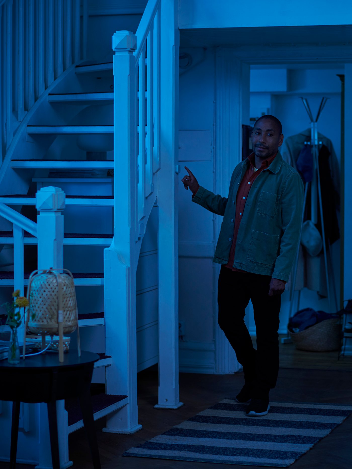 Fjärrkontrollen STYRBAR ligger på ett sidobord och lampan TRÅDFRI med färgat och vitt spektrum färgar rummet blått för att visa smart belysning från IKEA.