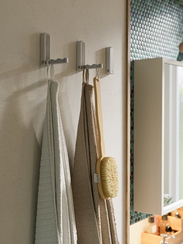 Teil einer Wand mit mehreren BJÄRNUM Haken, an denen Kleidung und Accessoires zu sehen sind. Der dritte Haken ist eingeklappt.