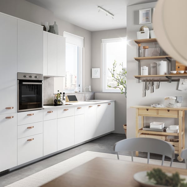 Piccola cucina bianca con frontali e ante VEDDINGE bianco, piastrelle arancioni/gialle, piano cottura e binario con alcuni utensili da cucina appesi - IKEA