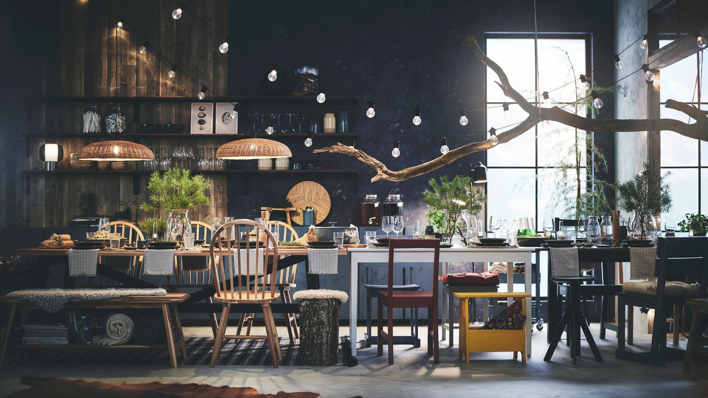 Une longue table à manger remplie de vaisselle, entourée de différentes chaises prêtes à accueillir les invités, avec des lumières suspendues au plafond.