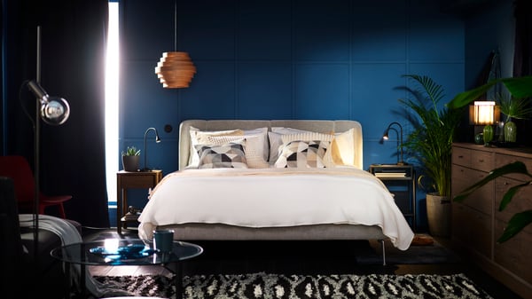 Un lit deux places matelassé TUFJORD dans une pièce bleue recouvert d’un ensemble de couette OFELIA VASS 3 pièces blanc et de coussins revêtus de housses de coussin SANELA.