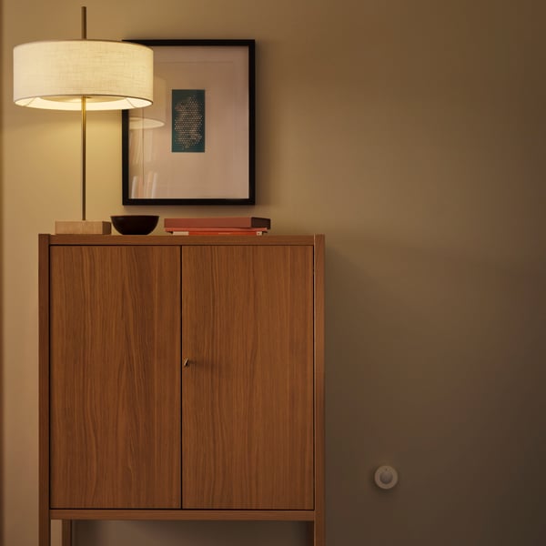 A MYGGSPRAY wireless motion sensor is mounted on a wall near a STOCKHOLM 2025 cabinet with two doors.