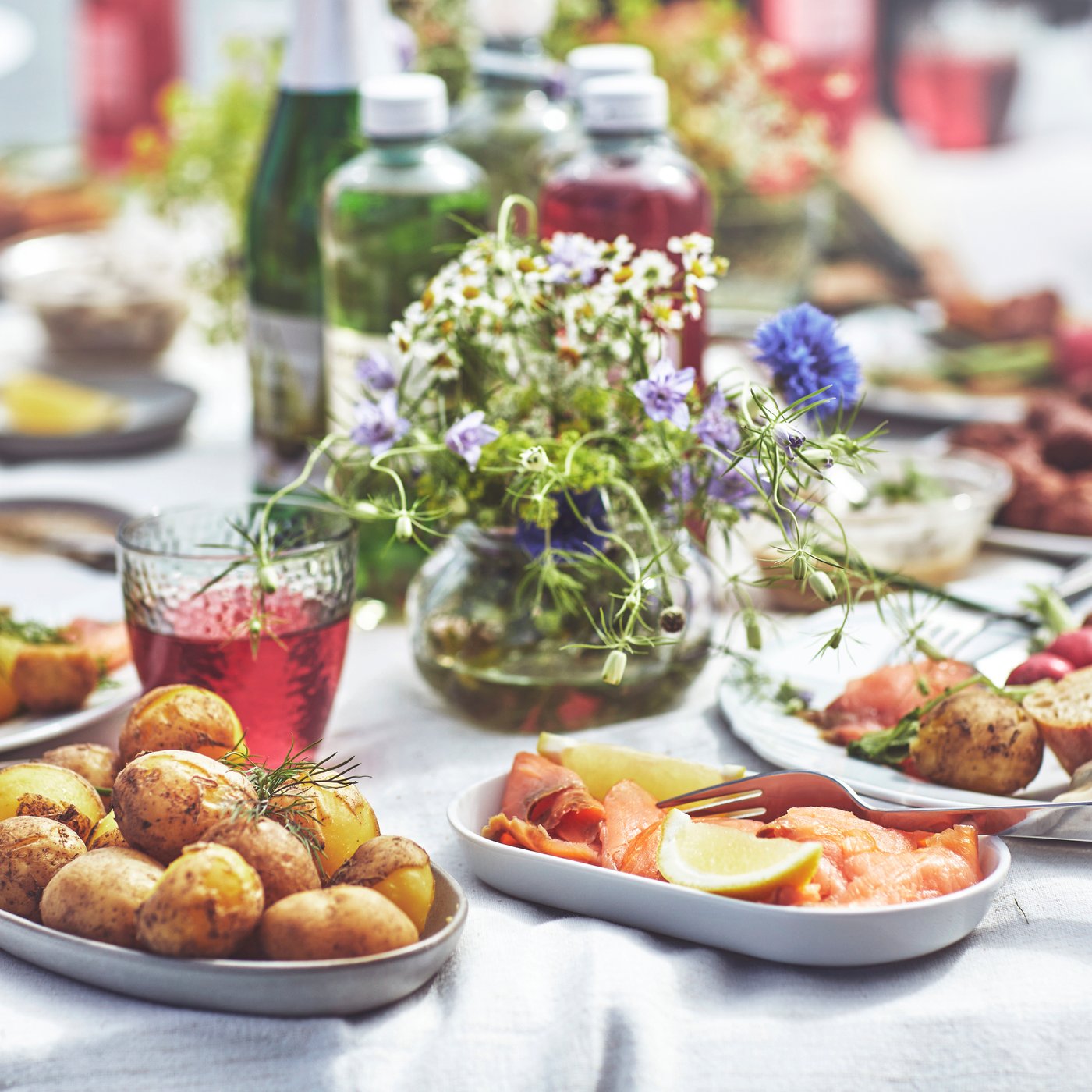 Gedeckter Tisch mit vielen Teller und Servierplatten und Blumen.