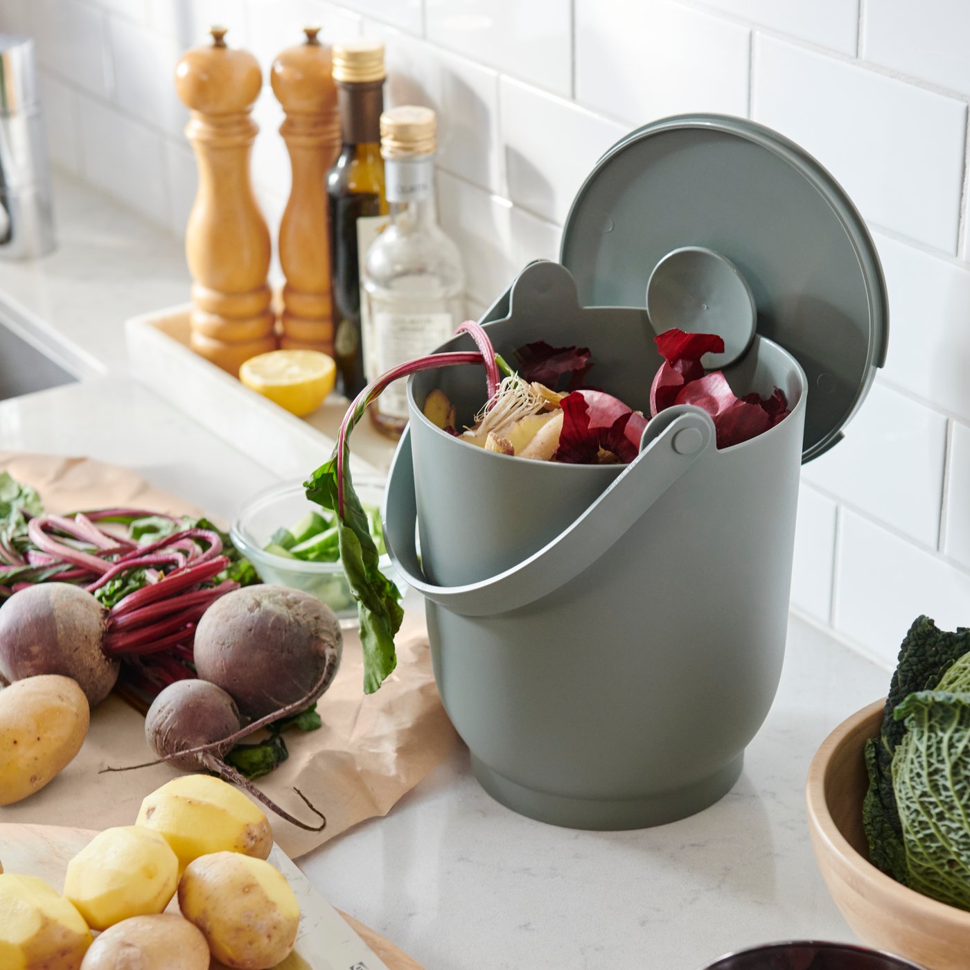 Keittiön valkoisella tasolla, juuresten vieressä on harmaanvihreä FARMARKVAST-biojäteastia